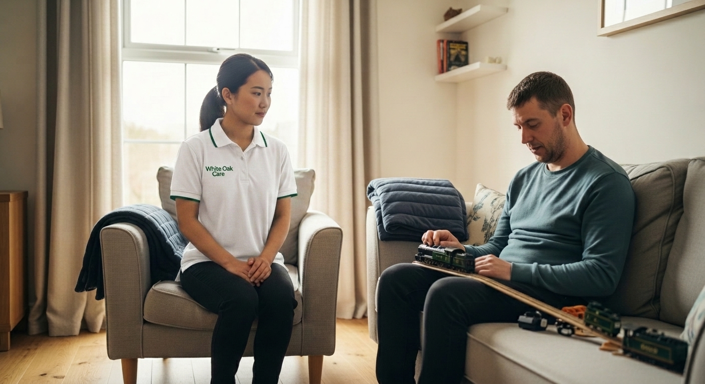 A White Oak Care support worker quietly present beside an autistic resident engaged with a personal interest in the sensory-aware lounge of a UK supported living home.